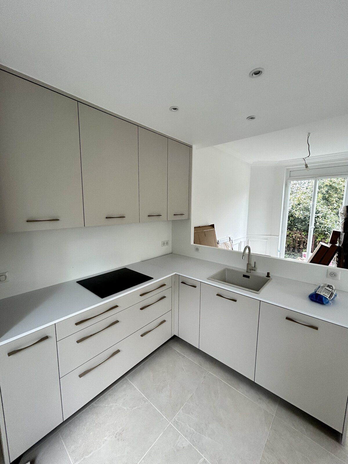 Cuisine après rénovation : meubles taupe et blancs, plan de travail clair, plaque à induction