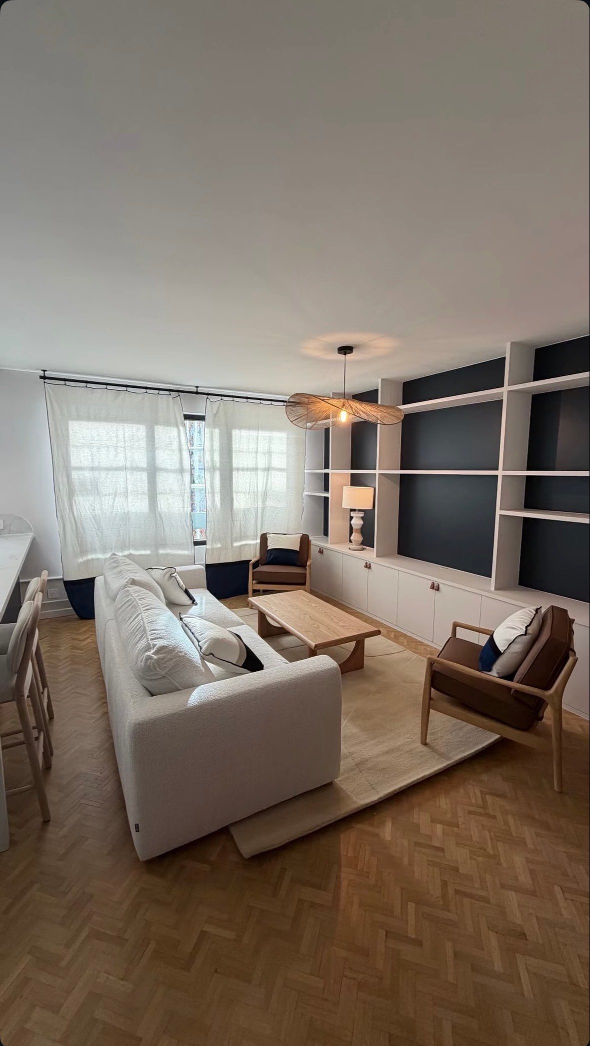 Salle de vie du projet Paris 12 : bibliothèque sur mesure bleu nuit, canapé blanc et parquet point de Hongrie